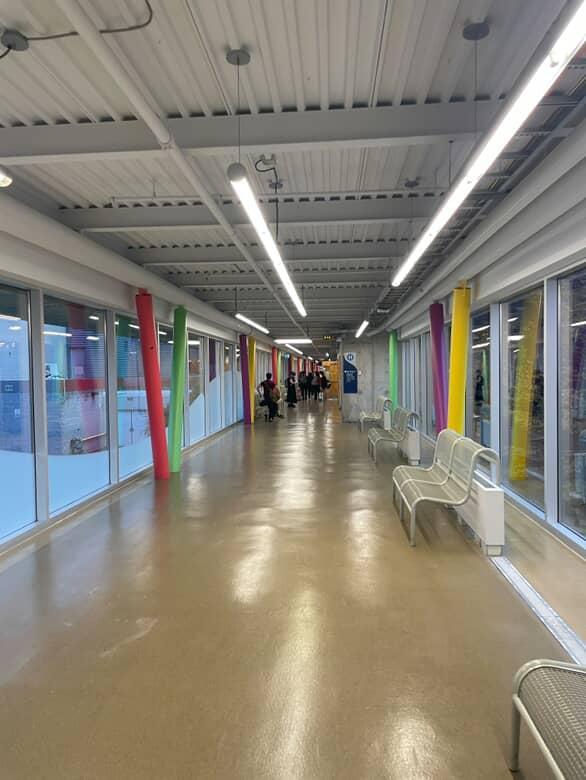 Space 2 – Colorful Walkway (By the Dance and Music Rooms)

This hallway connects to the cafeteria and marquee, and it’s the one me and my friends always take to go grab food.
I can always hear music and dance practice from the nearby rooms, which gives it a fun and lively energy.

Style: Modern, creative, and full of color.
What I see:

Colorful beams (red, yellow, green, purple)
Glass walls that let in tons of natural light
Metal ceiling with long strip lights
Overall vibe: Bright, active, and creative and it really matches the kind of students who hang around there.

 <div class='container'><iframe class='responsive-iframe' src='https://www.youtube.com/embed/tgbNymZ7vqY'></iframe></div>